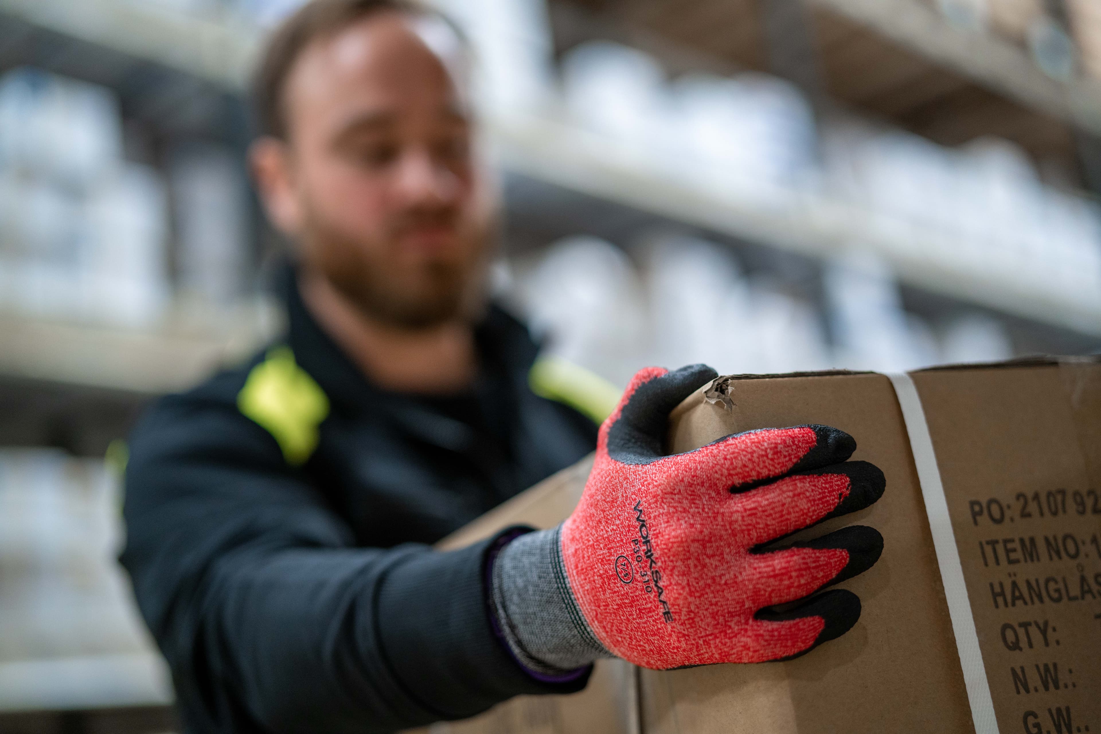 Närbild på person med handskar från Worksafe som bär en låda